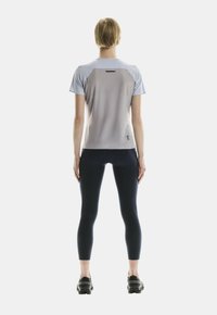 Helltürkisfarbenes SportT-Shirt mit einem Farbverlaufsdesign, kurzen Ärmeln und einem kleinen Logo unten links. Kombiniert mit schwarzen Leggings und Schuhen.