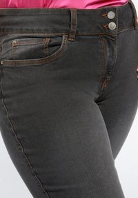 Tmavě šedé džíny z denimu s oranžovým prošitím, dvěma předními kapsami a dvěma knoflíkovými zapínáními v pase. Měkká textura, slim-fit design.