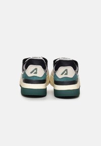 Sneakers con una combinazione di colori verde e nero, caratterizzati da un retro testurizzato beige e nero, suola in gomma e dettaglio del logo sul tallone.