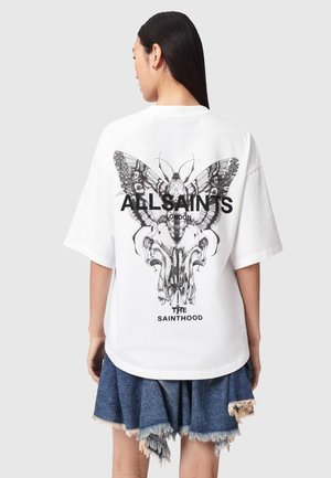 Woman wearing white oversized T-shirt with detailed black butterfly and skull graphic and text "ALLSAINTS LONDON THE SAINTHOOD" on back.