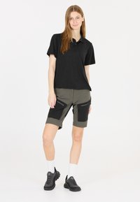 Svart polo skjorta, beige shorts med svarta detaljer och dragkedjefickor, ihop med svarta sneakers och vita ankelsockor.
