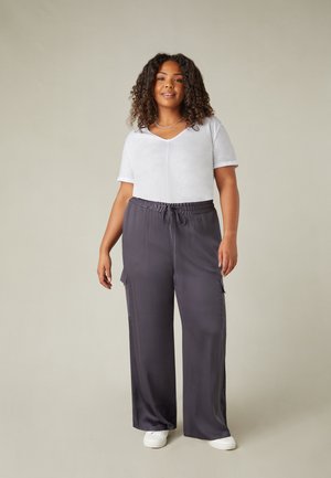 Haut gris clair à manches courtes en V associé à un pantalon large gris foncé avec une taille élastique et des poches latérales. Baskets blanches.