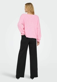 Svetlo roza puhasta pulover s dolgimi rokavi, v par z visokim pasom in širokimi črnimi hlačami. Pulover ima zaobljen rob in teksturiran zaključek.