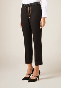 Pantalones negros a medida con dobladillo vuelto, combinados con tacones glitter con correa en el tobillo. Incluyen un cinturón negro con un detalle de cadena dorada.