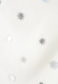 Tissu blanc parsemé de petits sequins ronds transparents cousus, reflétant la lumière sur le fond textile lisse.