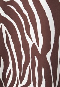 Tessuto marrone e bianco con un motivo a strisce zebra, caratterizzato da una texture liscia e larghezze di strisce variabili. Lo sfondo è di un bianco uniforme.