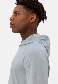 Maglietta con cappuccio azzurro chiaro dalla texture morbida. Presenta maniche raglan e un piccolo logo dettagliato sulla manica sinistra.