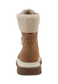 Barna velúr bokacsizma világos bézs műszőrme szegéllyel, oldalsó cipzárral és fehér texturált talppal. A cipő márkás sarok díszítéssel rendelkezik.