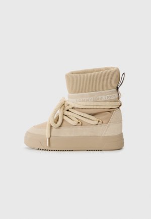 Beige høye støvler med ribbestrikket krage, semsket og glatt tekstiloverdel, rund tå og snøring med gullfarge detaljer.