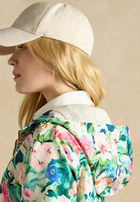 Bloemmotief met capuchonjack in pasteltinten met groene, roze en blauwe kleuren. Zacht stof met een witte kraag en gouden ritsaccenten.