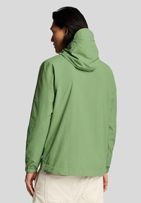 Chaqueta ligera de color verde claro con capucha, que presenta puños elásticos y un ajuste relajado. Textura suave, sin patrones visibles ni detalles de hardware.