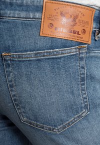 Tasca posteriore di jeans Diesel in denim blu con patch in pelle marrone del marchio cucito sopra la tasca.