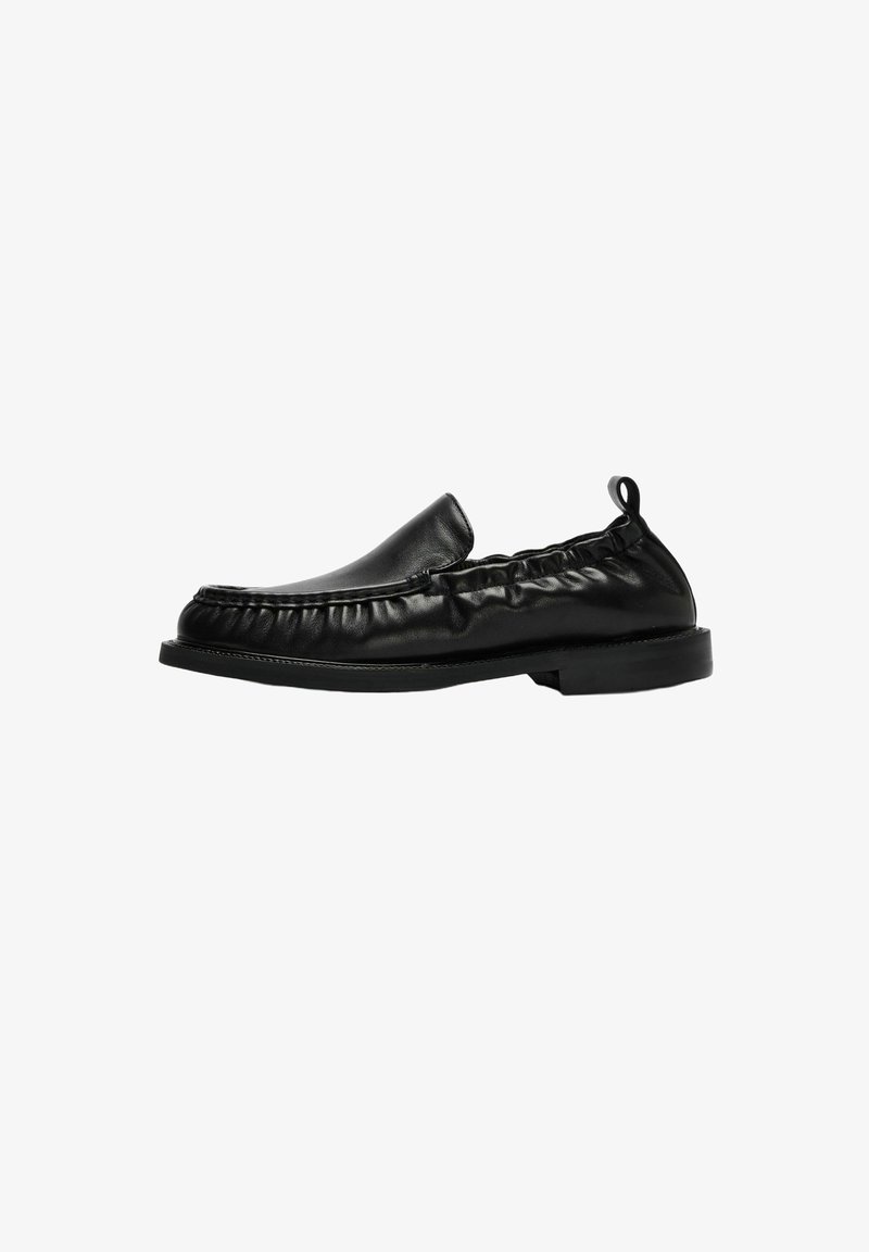 Chaussure noire en cuir à enfiler avec des côtés froncés, un bout rond, une semelle plate et une languette de tirage côté talon.