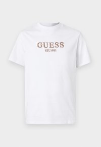 T-shirt bianca in cotone con maniche corte, caratterizzata da logo ricamato "GUESS" e dettaglio "EST. 1981" in marrone sul davanti. Vestibilità regolare.