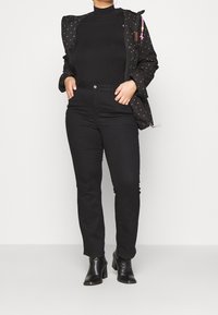 Czarna, wzorzysta kurtka z kapturem, nałożona na czarny golf oraz dopasowane czarne dżinsy. Noszona z czarnymi botkami za kostkę.