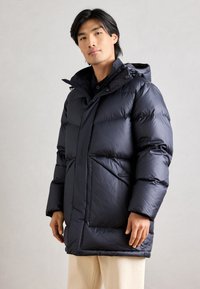 Casaco puffer azul-marinho com colarinho alto, fecho frontal com botões e dois grandes bolsos laterais. Apresenta uma textura suave e brilhante.