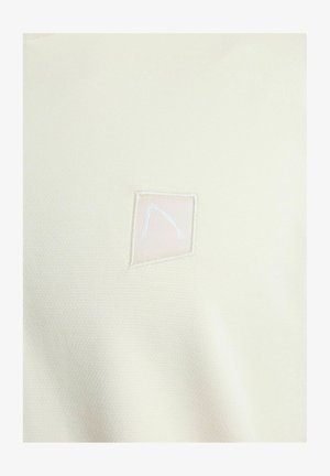 Svetlobéžová košeľa z textúrovaného materiálu, s malým štvorcovým logom v jemnej ružovej farbe s bielym okrajom. Jednoduchý, minimalistický dizajn.