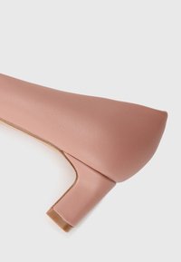 Pink leather high-heeled shoe with a block heel, smooth texture, pointed toe, and minimalistic design. Side view against a white background.