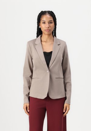 Lys beige blazer med spiss krage og enkelt knappelukking, med to frontlommer og en glatt stoffoverflate. Kombinert med bordeaux bukser.