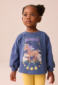 Niebieska bluza polarowa z grafiką jednorożca i kolorowymi akcentami. Długie rękawy z ściągaczami. Widać parę żółtych legginsów.