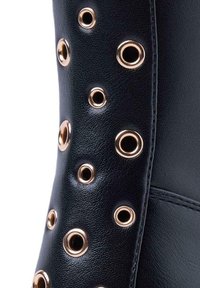 Stivale in pelle nera con occhielli dorati di diverse dimensioni disposti lungo il lato, che mettono in risalto la texture e i dettagli.