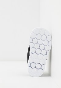 Sål i vitt gummi med hexagonalt mönster, placerad vertikalt mot en vit vägg, svart ovandel delvis synlig.