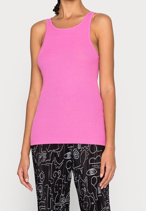 Kobieta ubrana w różowy, bezrękawnik prążkowany i czarne spodnie z białymi abstrakcyjnymi wzorami linii.