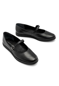 Zapatos planos de cuero negro con punta redonda, una cinta estrecha a través del empeine y superficie texturizada. La suela es plana con una ligera curvatura.