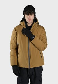 Giacca isolata marrone con cappuccio, zip frontale e tasche laterali. Abbinata a guanti neri e un cappello lavorato a maglia. Tessuto liscio.