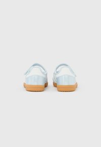 Par ljusblå och vita sneakers för småbarn med bruna gummisulor, sedd bakifrån mot en enfärgad vit bakgrund.