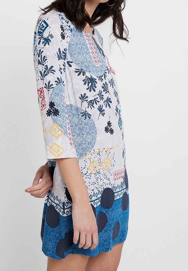 Robe tunique multicolore avec des manches trois-quarts, ornée de motifs floraux et géométriques en bleu, rouge, jaune et blanc sur un fond clair.