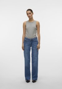Top sin mangas gris combinado con jeans de cintura alta y pierna ancha azules. Tejido suave con textura clásica de denim. Tacones negros de punta para aportar contraste.