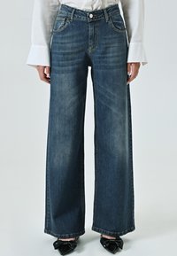 Brede spijkerbroeken in donkerblauwe denim, met een aansluitende taille, vijf zakken en een subtiele vervaagde textuur. Gestyling met schoenen met zwarte strikdetails.