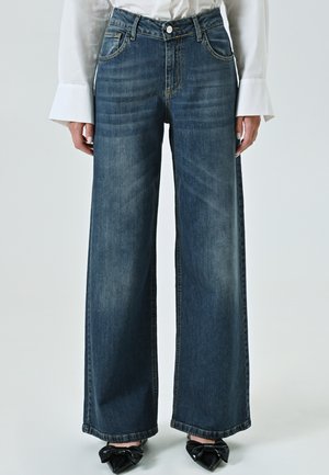 Wide-leg jeans in dark blue denim, featuring a fitted waist, five-pocket design, and subtle faded texture. Styled with black bow detail shoes.
