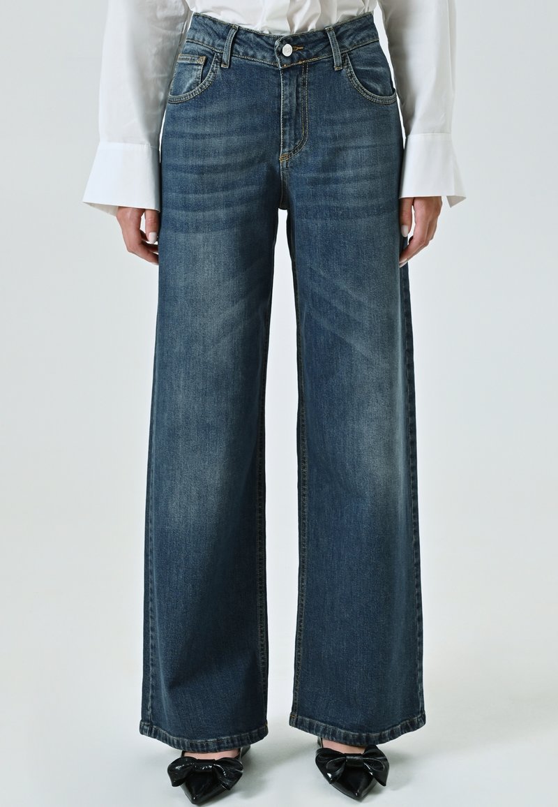 Brede spijkerbroeken in donkerblauwe denim, met een aansluitende taille, vijf zakken en een subtiele vervaagde textuur. Gestyling met schoenen met zwarte strikdetails.