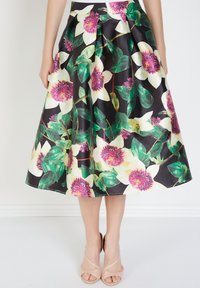 Falda midi floral con grandes flores blancas y rosas sobre un fondo negro, con pliegues y una textura suave. Complementada con sandalias beige.