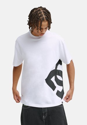 Biały, krótki rękaw T-shirt z dużym czarnym nadrukiem po lewej stronie. Wykonany z bawełny, ma okrągły dekolt i luźny krój.