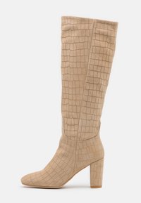 Bottes hauteur genou en daim beige avec un motif croco texturé, un bout pointu et un talon bloc pour plus de stabilité.