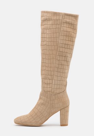 Bottes hauteur genou en daim beige avec un motif croco texturé, un bout pointu et un talon bloc pour plus de stabilité.