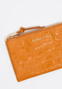 Orange patent leather zip wallet featuring a crocodile texture, gold "BIMBA Y LOLA" branding, and a matching zipper pull.