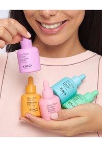 Seis frascos de suero sostenidos en una mano: rosa, naranja, verde y azul, todos con tapas de cuentagotas. Cada uno tiene etiquetas distintas y formas redondeadas.