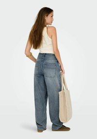 Höga, vida blå denimjeans med två bakfickor, i kombination med en beige linne topp och håller en mjuk gräddfärgad tote-väska.