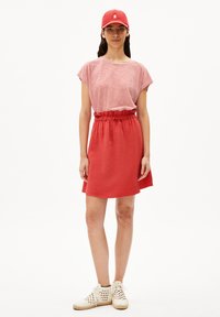 Gorro rojo, camiseta de rayas rojas y blancas de manga corta, falda roja con cintura elástica y zapatos blancos con cordones. Atuendo casual con una estética deportiva.