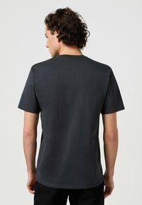 Camiseta de algodón gris oscuro con manga corta, cuello redondo, textura suave y corte relajado. Sin logotipos ni patrones visibles.