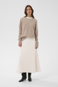 Beežist kudumist pikkade varrukatega kampsun koos valge põrandapikkuse seelikuga. Lõpetatud mustade pahkluu saabastega kontrasti loomiseks. Lihtne ja puhas disain.