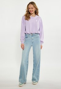 Fioletowy, oversize sweatshirt z małym białym logo serca, w połączeniu z jasnoniebieskimi spodniami o szerokich nogawkach. Gładki materiał, luźny krój i swobodny styl.