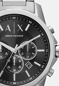 Roostevabast terasest kella kronograaf musta tahhiga, hõbedaste tunniindikaatorite, kolme alatahhi ja kuupäeva näidikuga kell 6 positsioonil.