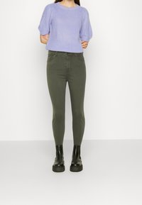 Lichtpaarse gebreide trui met korte, opbollende mouwen, gecombineerd met hoge groene skinny jeans en zwarte platform enkellaarsjes.