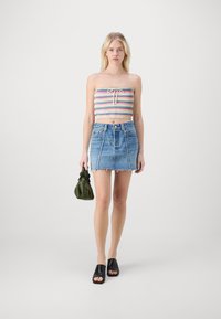 Top bandeau lavorato a maglia multicolore con dettaglio a fiocco, abbinato a una mini gonna di jeans azzurri chiari con orlo sfilacciato. Sandali neri e borsa verde.