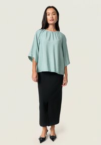 Top azzurro chiaro e leggero con scollatura rotonda e maniche ampie, abbinato a una gonna nera aderente con spacco frontale.